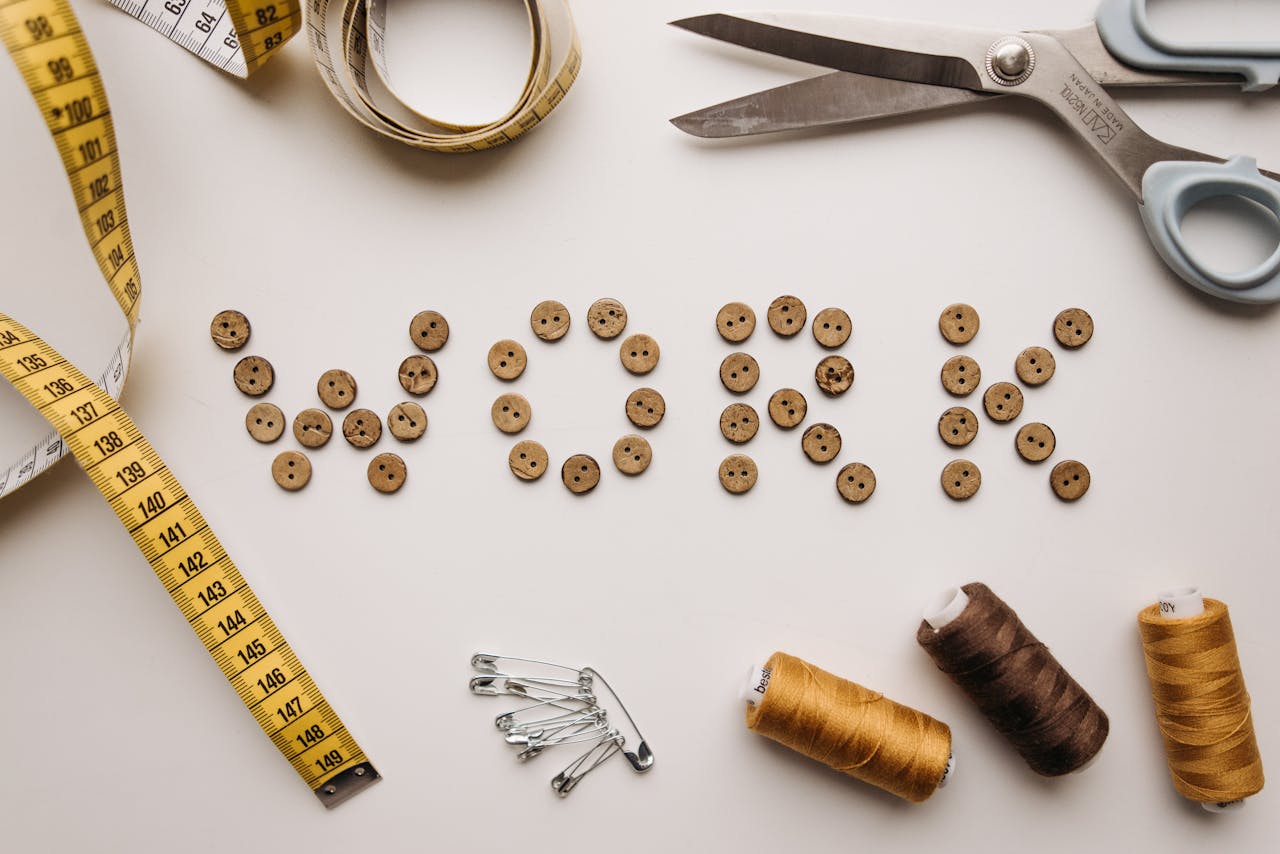 Sewing concept featuring buttons spelling 'work' surrounded by sewing tools on a flat lay.