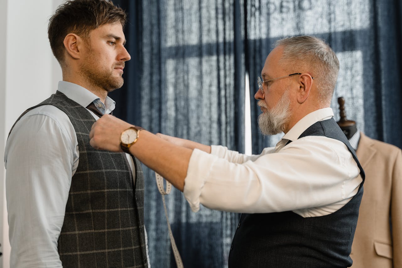 Professional tailor measuring a client for a custom suit in a workshop setting.